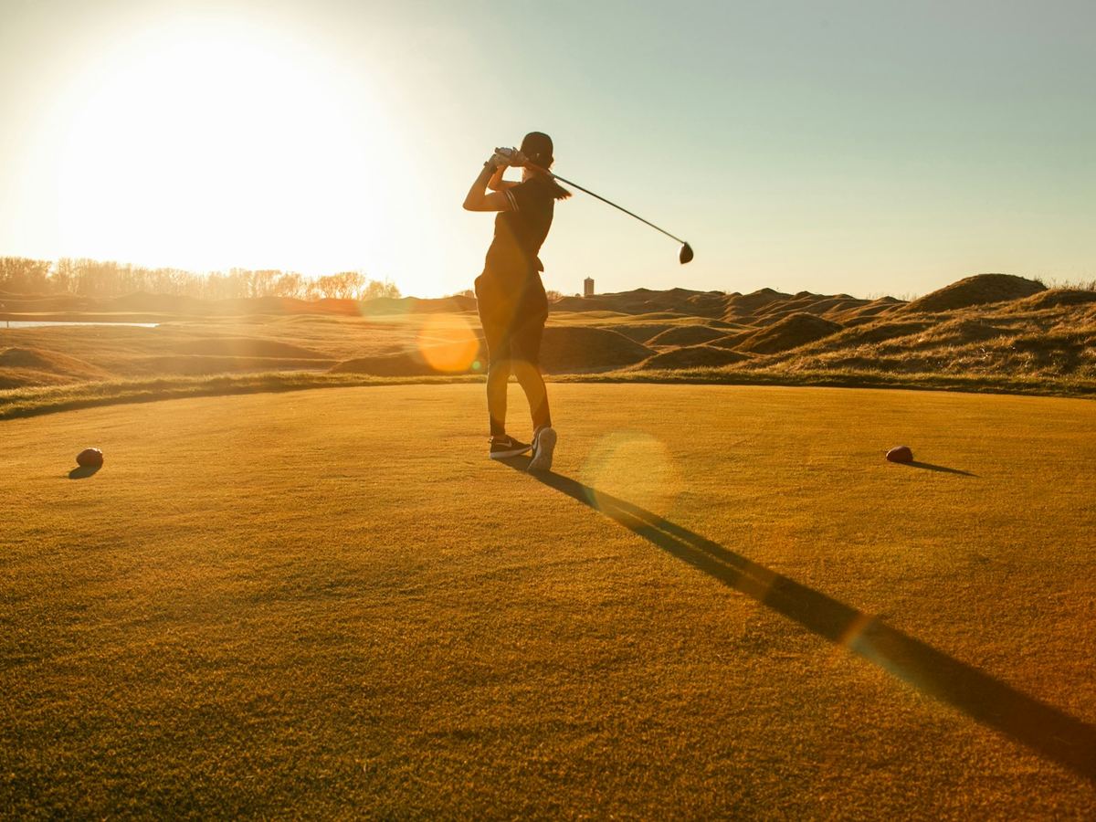 Golfer swinging at sunset on a golf course